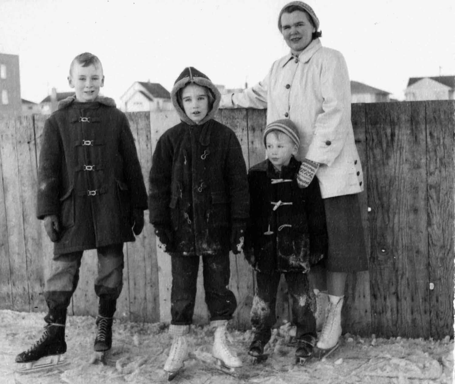 Thelma Pepper in her 30s with her three children, all in skates, standing in front of old ice rink fence.