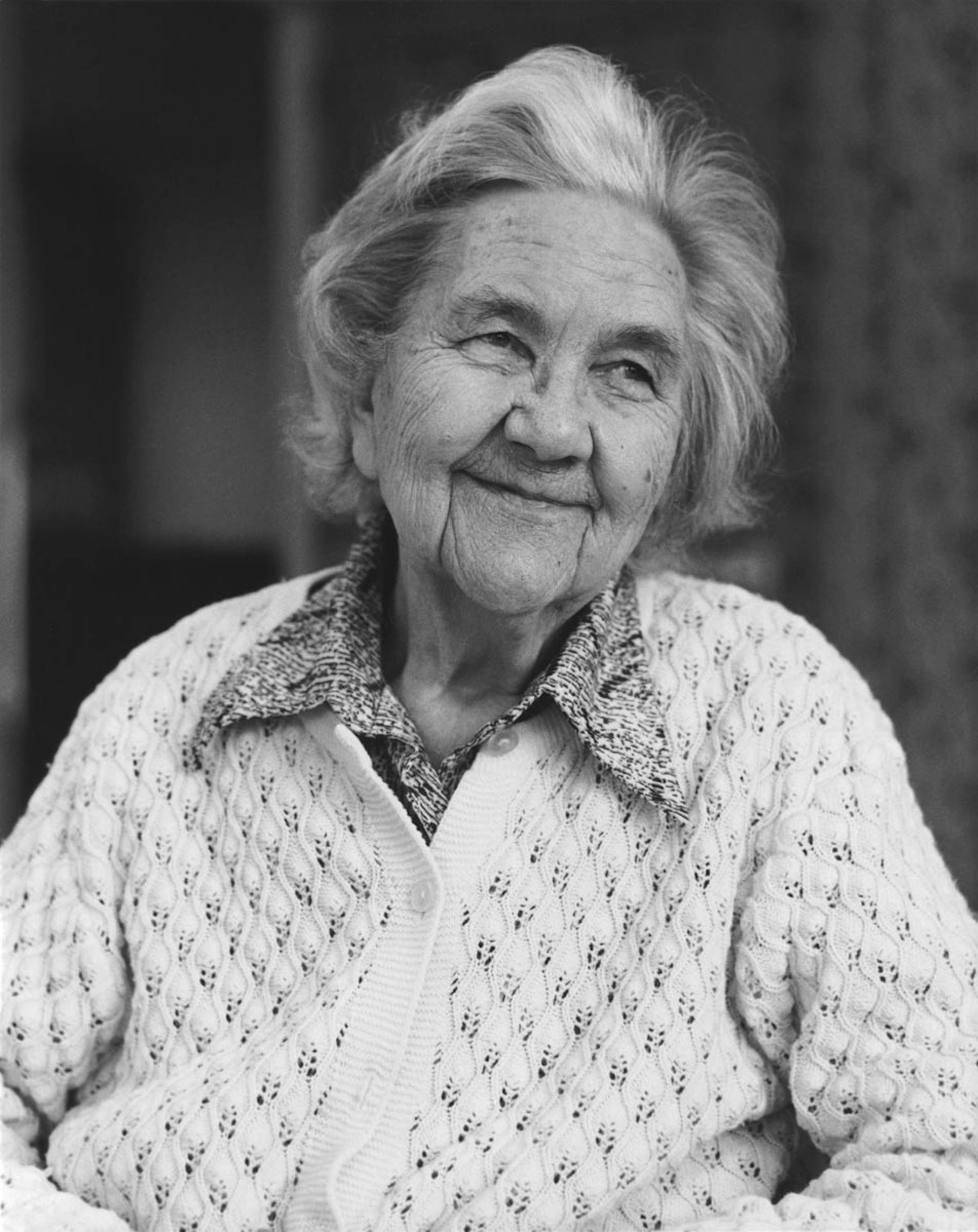 Black and white photo of elderly woman smiling and glancing off to the side.
