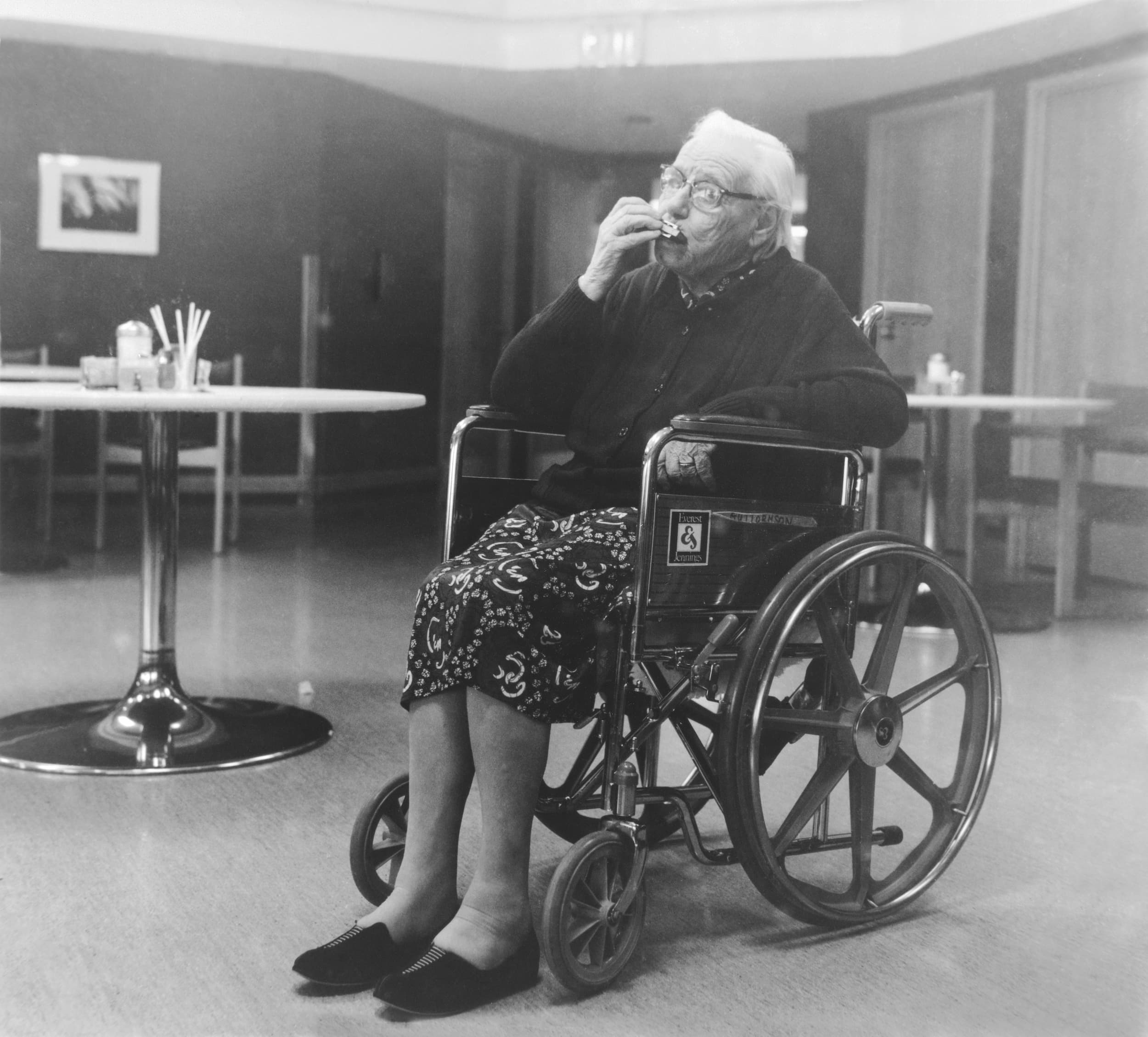Black and white photo of elderly woman in wheelchair playing harmonica.