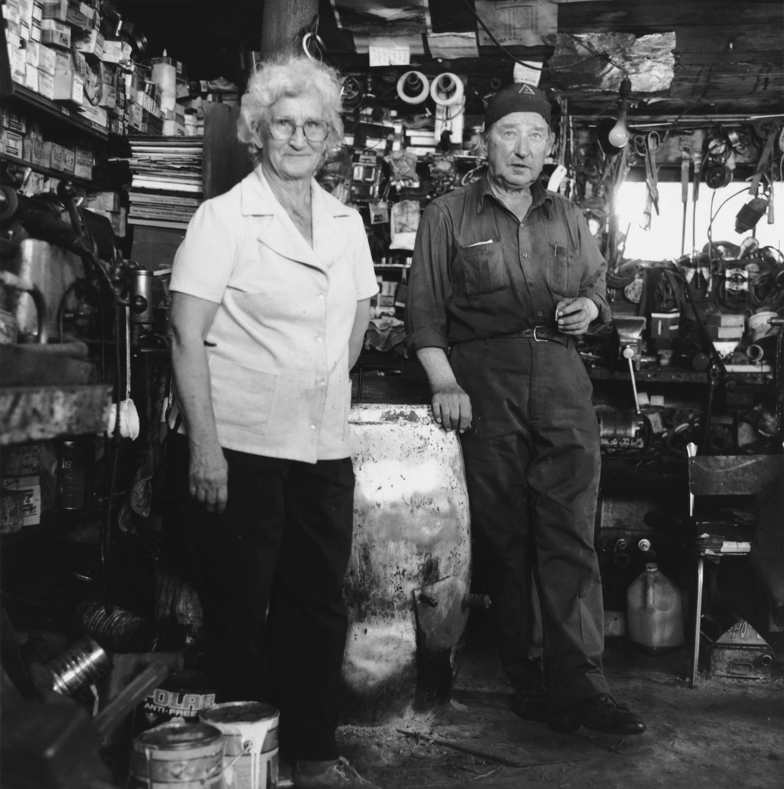 Black and white photo of elderly woman and man inside the man’s very small work shed.