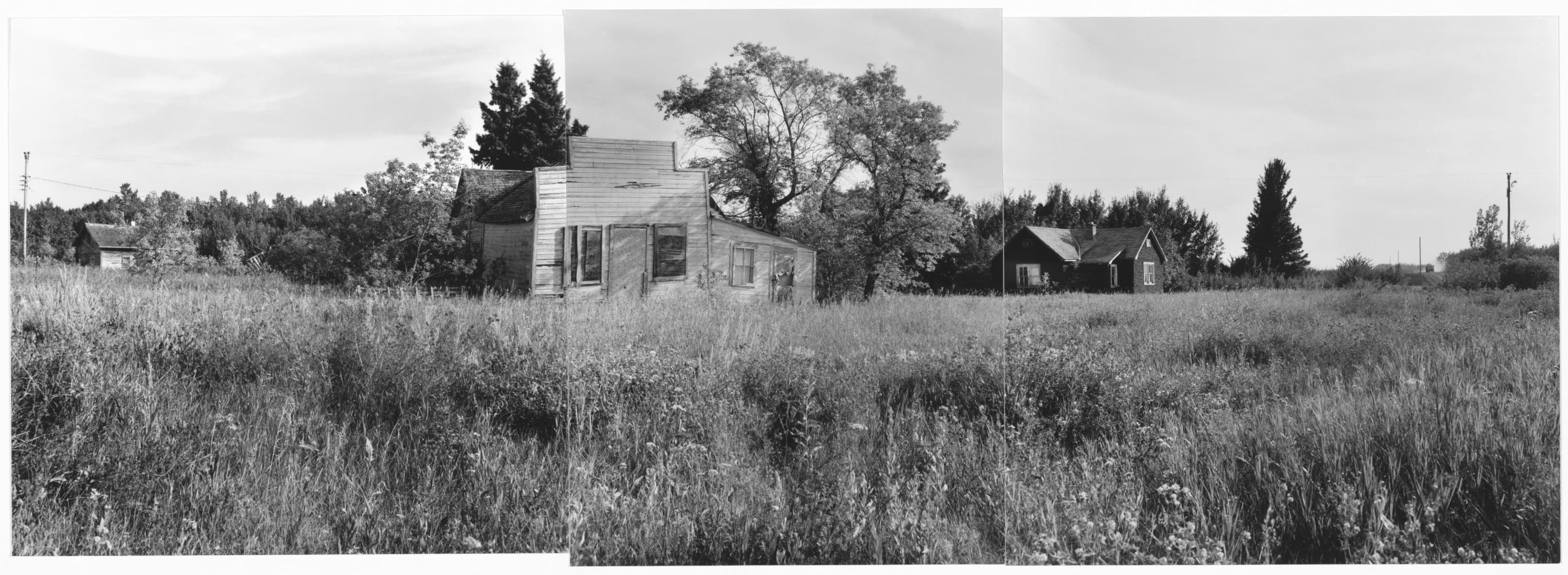 Black and white three panel panorama of an old school building in the centre sounded by grass and flowers and two smaller buildings at each end.