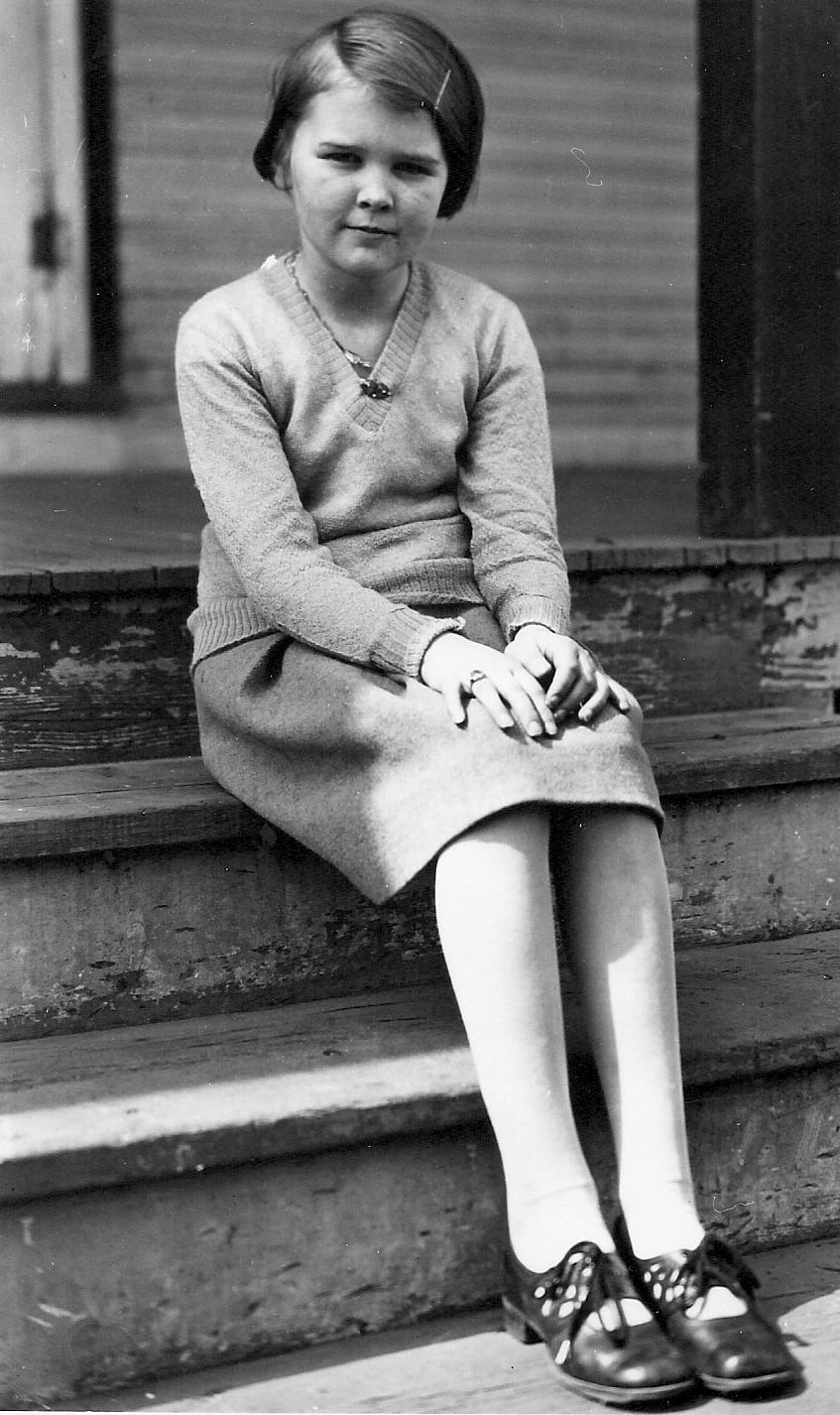 Closeup of Thelma Pepper about 10 years old sitting on old wooden steps in front of a building.